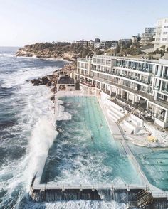 an aerial view of a large swimming pool next to the ocean with buildings in the background