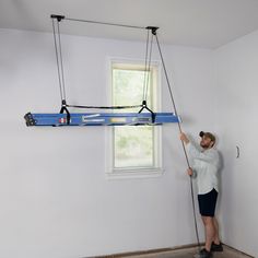 a man holding onto a ladder in the corner of a room with a window behind him