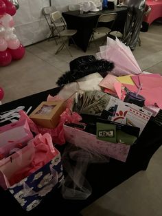 the table is covered with pink and white balloons, gift bags, and other items