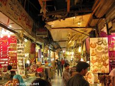 people are walking through an open market with many items on the shelves and in front of them