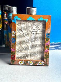 an old book page frame with flowers and clouds in the middle is sitting on a table next to cans