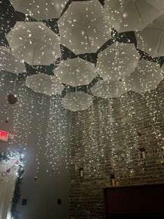 several white umbrellas hanging from the ceiling in a room with brick walls and lights