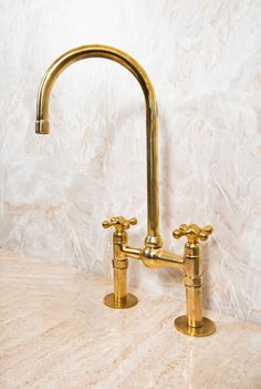 two brass faucets on a marble counter top