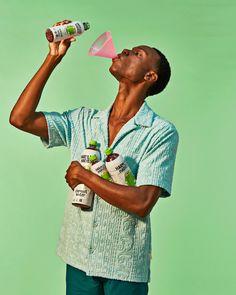 a man drinking from a bottle while standing in front of a green background