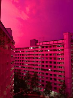 the sky is pink and there are buildings in the foreground with lights shining on them