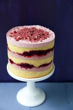 a cake with red and yellow frosting sitting on top of a white pedestal next to a blue wall