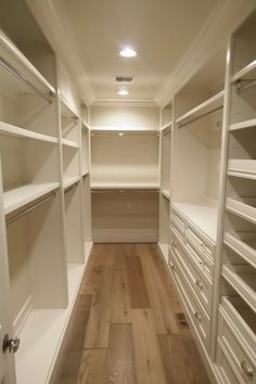 an empty walk - in closet with white shelves and drawers on each side, along with wooden flooring