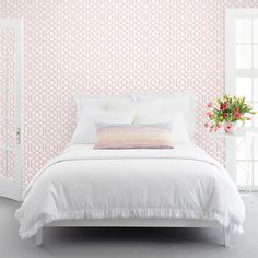 a white bed sitting in front of a window next to a vase with flowers on it