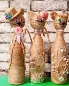 three cats made out of burlocks with flowers on their heads and tails, standing in front of a brick wall