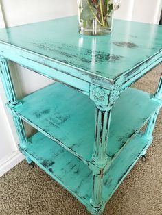 an old blue table with flowers in a vase on top and carpeted flooring