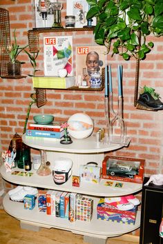 a shelf with books, magazines and other items on it in front of a brick wall