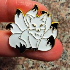 a white and black fox pin sitting on top of a persons finger