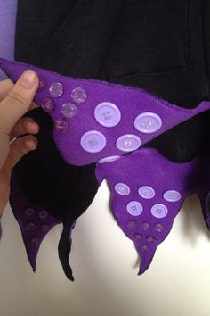 someone is sewing something with buttons on the purple fabric and black material that has been sewn together