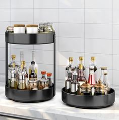 two black containers with silver and gold items in them on a white counter next to a sink