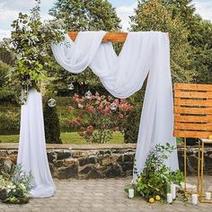 an outdoor wedding setup with white drapes and greenery on the side, surrounded by stone walls