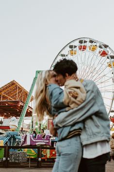 a man and woman kissing in front of a ferris wheel at an outdoor fairground