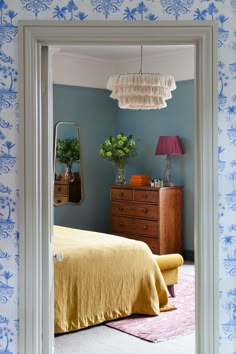 a bedroom with blue walls and yellow bedspread on the bed is seen through an open door