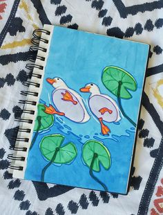 a notebook with two ducks floating on top of water lilies and lily pad leaves