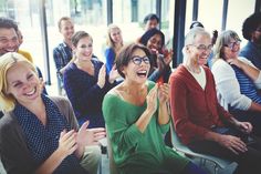 a group of people sitting next to each other in front of a glass wall with their hands up