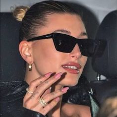 a woman wearing sunglasses and holding her hand up to her face as she sits in the back seat of a car