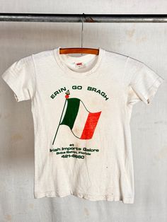 Authentic vintage t shirt with Hanes label for an Irish Imports shop in Florida with a flag graphic and phrase. made in USA era : 1960s 70s material : cotton color : aged white, green/orange condition : distressed , visible signs of age and wear as seen in photos and may include spots, small holes, and other patina size : tagged 12 approx childs large to xlarge, may fit an xsmall adult , please compare measurements below actual garment measurements : chest : 14" ptp length : 19" - - - - - - - - Vintage Band T Shirts 70s, 1970s Tshirt, Heritage School, 1970s Graphic Tee, Vintage Yellow T-shirt With Funny Print, Vintage Ireland, Vintage Souvenir Shirt, School Shirts, Vintage Tshirts