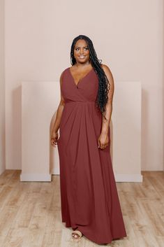 a woman in a long red dress standing on a wooden floor with her arms behind her back