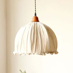 a white lamp hanging from a ceiling next to a plant in a potted planter