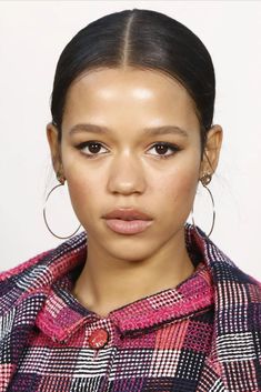 a close up of a person wearing a plaid coat and hoop earrings with her hair in a pony tail