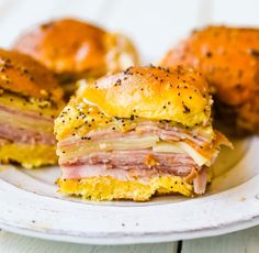 ham and cheese sandwich cut in half on a white plate with buns behind it