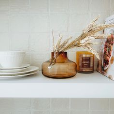 a white shelf topped with dishes and vases filled with flowers next to a book