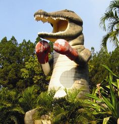 a large statue of a crocodile with boxing gloves on it's feet in front of trees