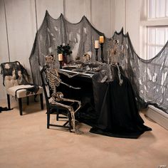 a dining room table covered in black cloths and skeleton chairs with candles on them