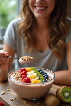 a woman smiles as she holds a spoon full of fruit and granola in front of her