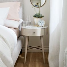 a small white table with a mirror on it next to a bed and two glasses