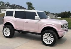 a pink truck parked in front of a house on a driveway with white tires and rims