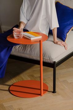 a woman sitting on a couch next to a table with a book and drink in it