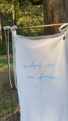 a white towel hanging from a clothes line with blue writing on it that says, welcome to our forever