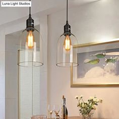 two clear glass pendant lights hanging over a dining room table with wine glasses on it