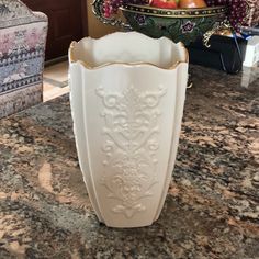 a white vase sitting on top of a counter next to a bowl filled with fruit