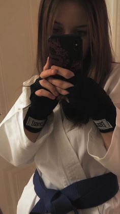 a woman taking a selfie with her cell phone while wearing karate gear and holding a black belt