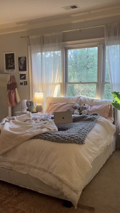 a laptop computer sitting on top of a white bed in a room with two windows