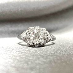 an old - fashioned diamond ring sits on top of a silver surface, with the center stone surrounded by smaller diamonds