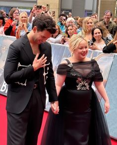 a man and woman walking down a red carpet with people in the background taking pictures