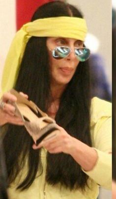 a woman with sunglasses and a yellow scarf around her head is looking at a purse