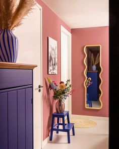 a vase with flowers sitting on top of a blue stool in front of a mirror