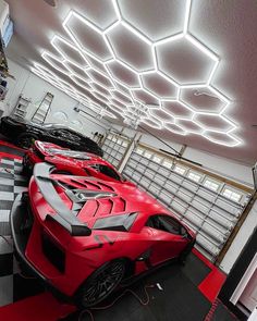 two red sports cars are parked in a garage with checkered flooring and lights