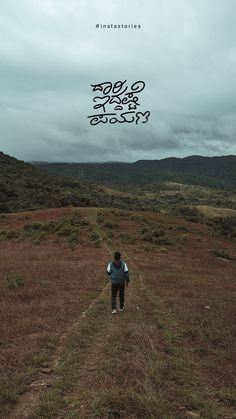 a man walking down a dirt road in the middle of a dry grass covered field