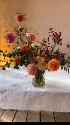 a vase filled with lots of flowers sitting on top of a white tablecloth covered table