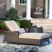 an outdoor chaise lounge with pillows on the back and in front of a house