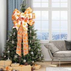 a decorated christmas tree in front of a window with presents under it and an orange bow